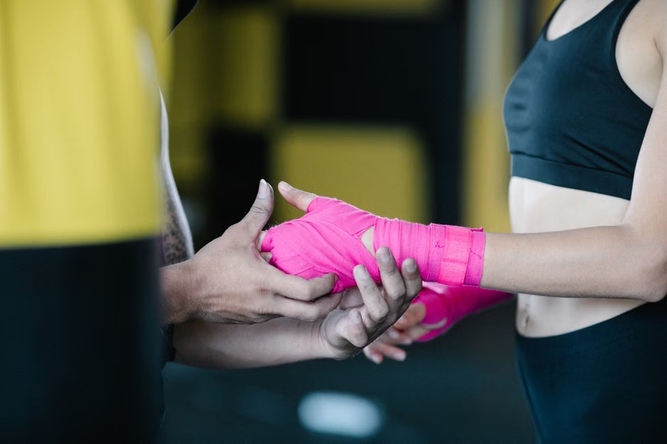 Coach wrapping a new member's hands in pink hand wraps before their first boxing class — welcoming beginner instruction — Legends Boxing