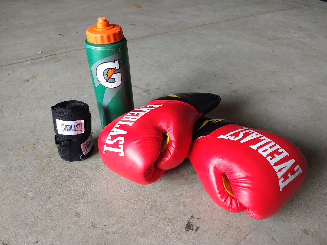 Everlast red boxing gloves, black hand wraps, and a Gatorade water bottle on a concrete floor — essential beginner boxing gear for women — Legends Boxing