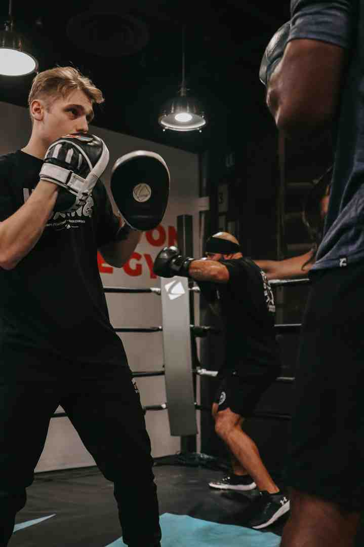 Young boxer in white bag gloves throwing a straight punch at focus mitts held by a coach inside a boxing ring — personalized mitt work training — boxing gym Layton Utah — Legends Boxing