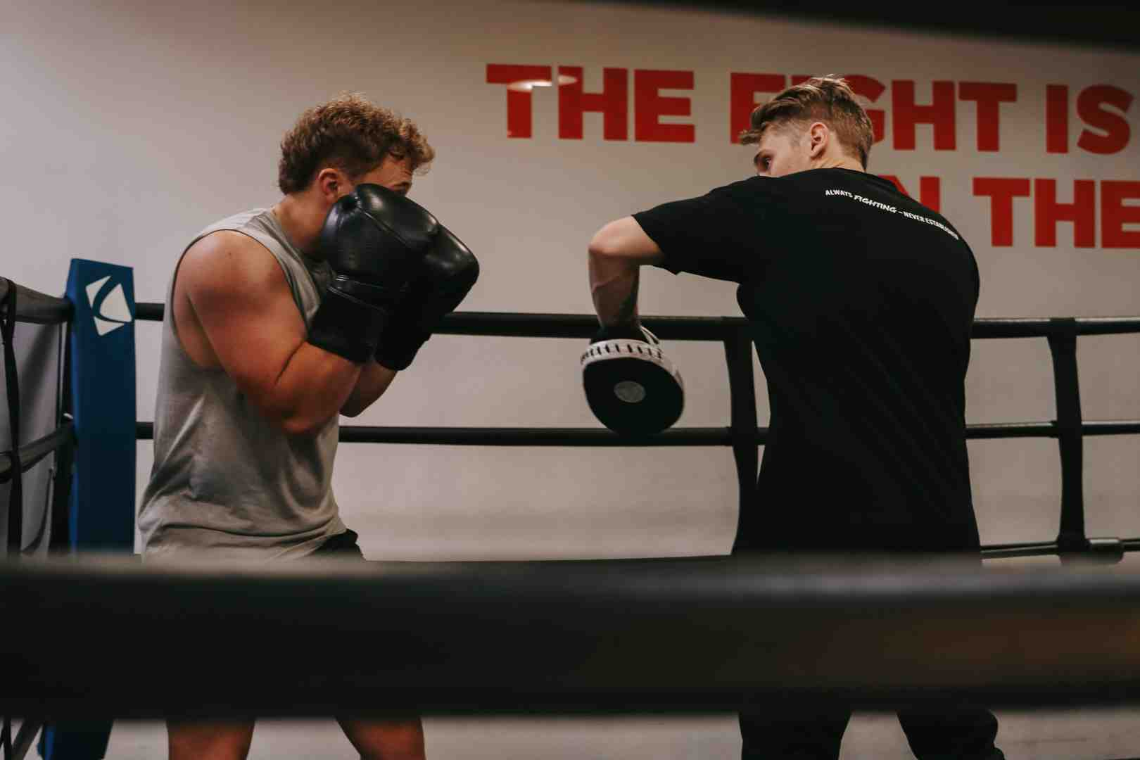 Legends Boxing coach working one-on-one mitts drill with a member inside the boxing ring — "THE FIGHT IS" mural visible behind them — personalized coaching at the boxing gym in Orem Utah