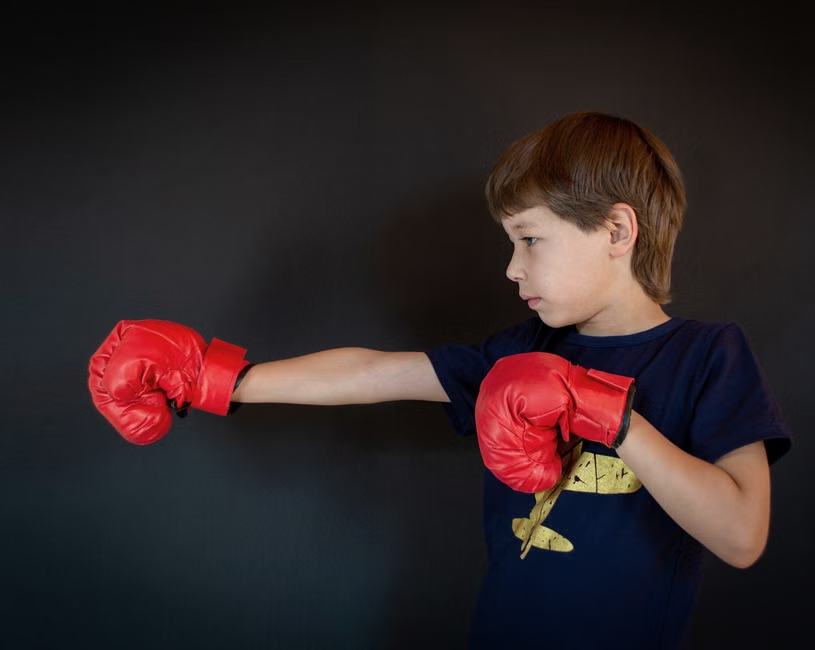 Young boy in a focused boxing stance throwing a straight punch with red gloves against a dark background — demonstrating proper form