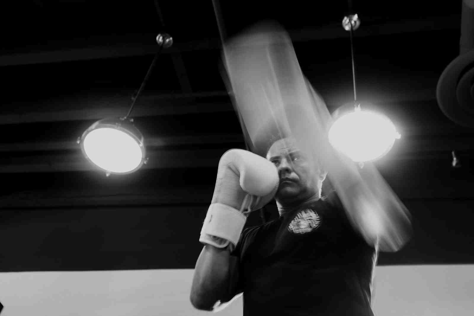 Dramatic black and white photo of a boxer in a Legends Boxing shirt throwing a punch with motion blur — gym lights illuminating the scene — capturing the explosive speed and power that defines the hardest punchers in boxing history