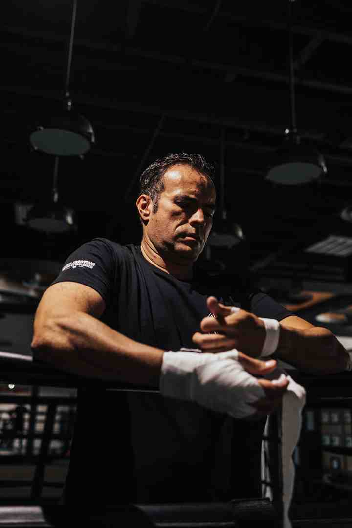 Athlete carefully wrapping hands with white boxing wraps at a boxing gym ring, focusing on preparation before training
