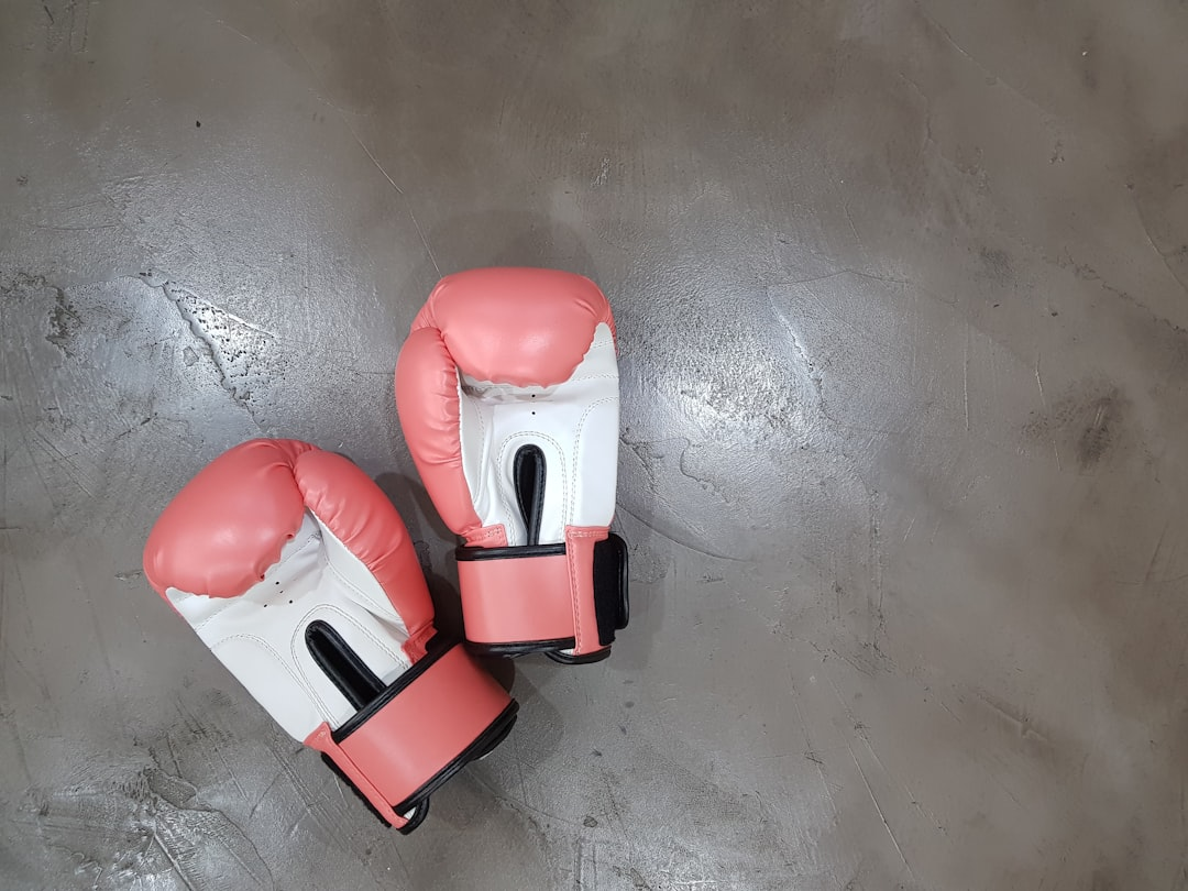 Two salmon-pink and white boxing gloves with Velcro closures resting on a grey concrete gym floor — youth/junior boxing gloves in a soft color — Legends Boxing